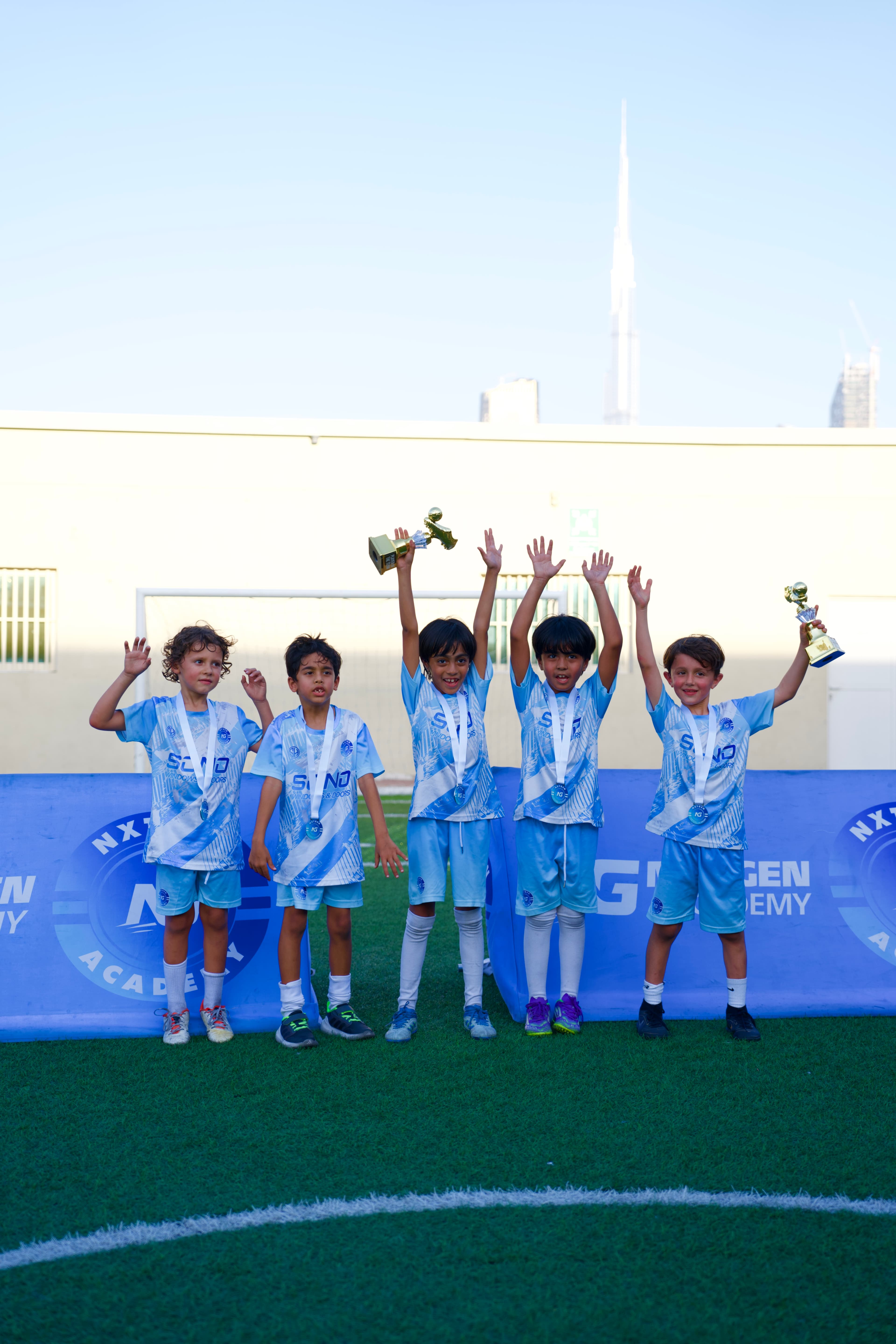 Young NXTGEN Holiday Camps players celebrate with medals and trophies.